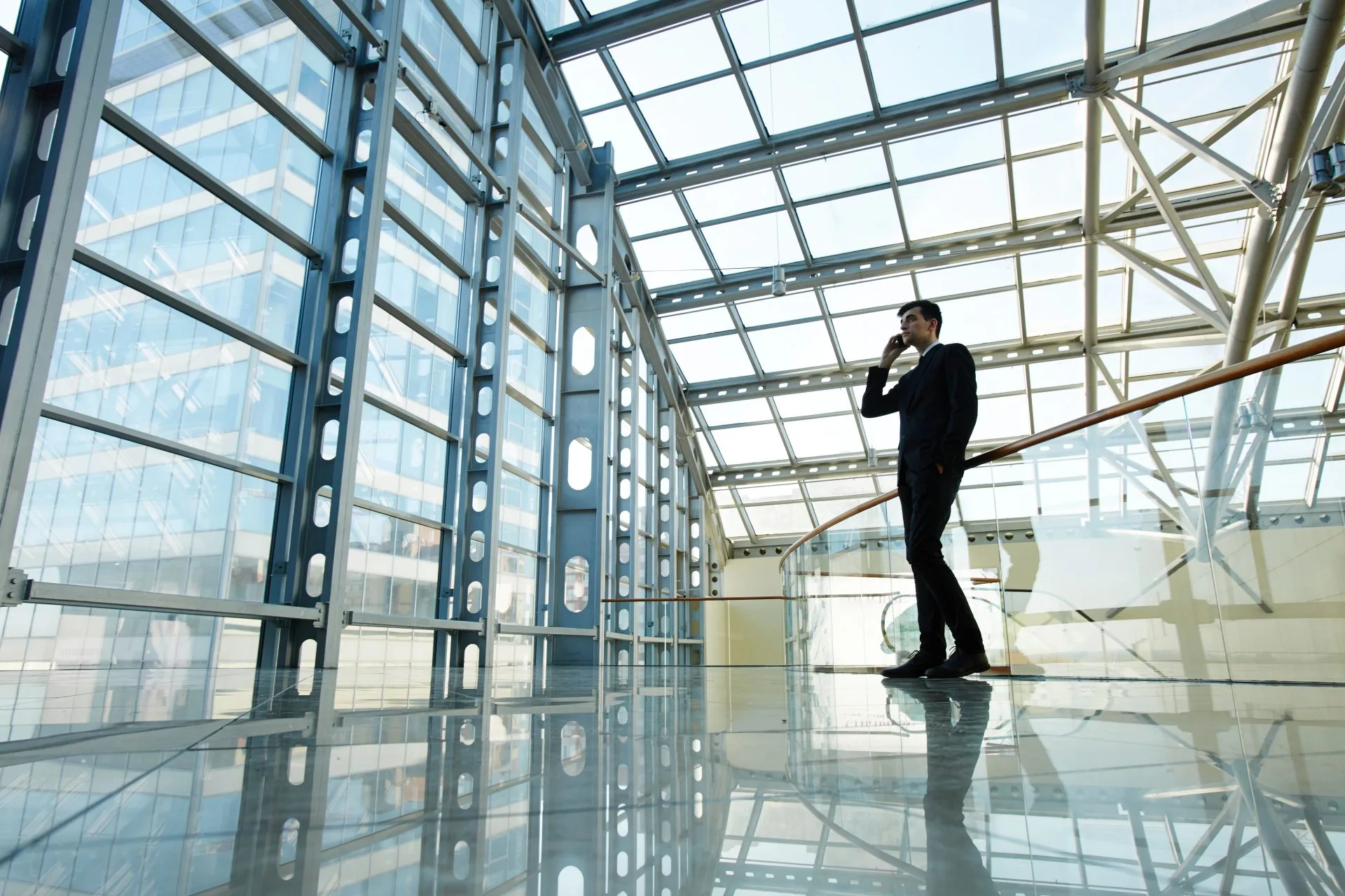 Man in a suit talking on his phone in a modern building with a glass-and-steel structure