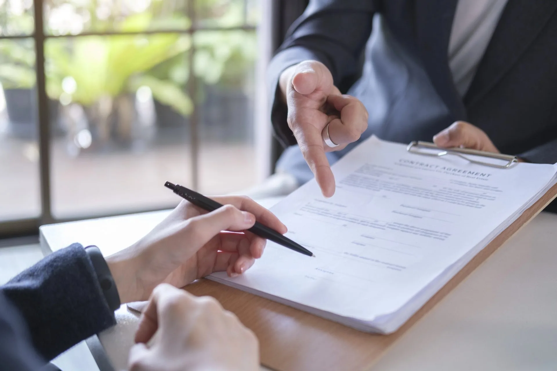 Two people reviewing a contract agreement document at a desk, one pointing to a clause while the other holds a pen