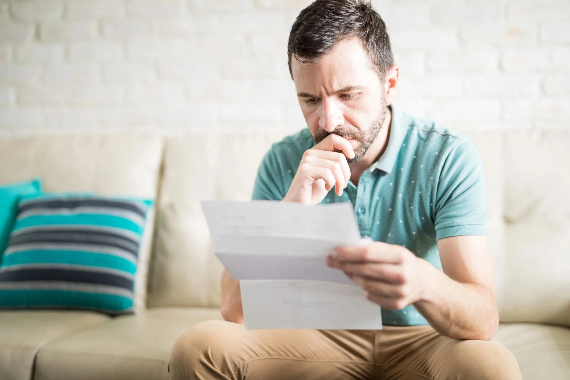 Man reading a document with a concerned expression while sitting on a couch at home