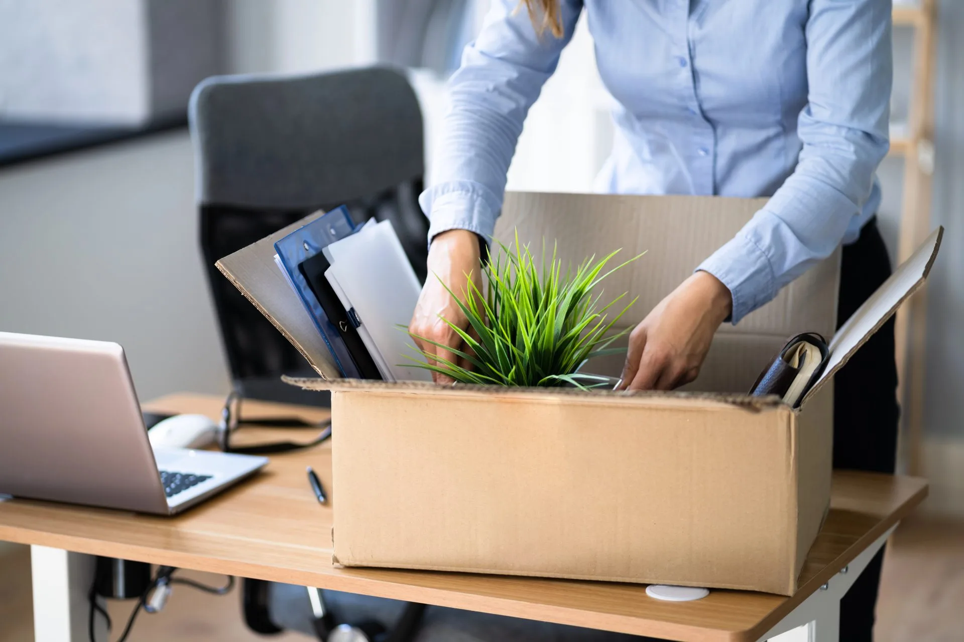 Person packing personal belongings into a cardboard box on an office desk after leaving a job